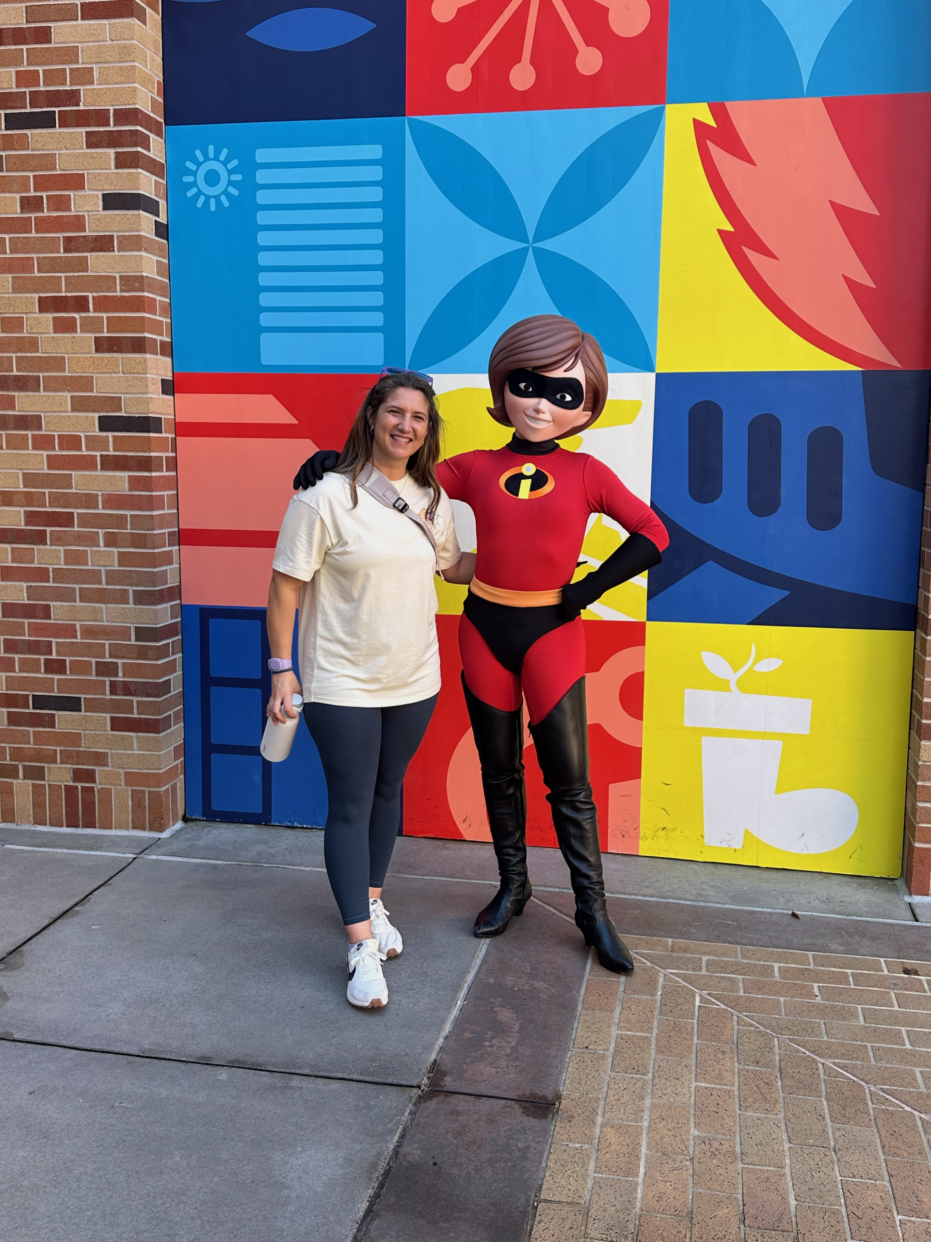 Danielle smiling with Mr. Incredible in front of a colorful mural at Disney's Hollywood Studios.