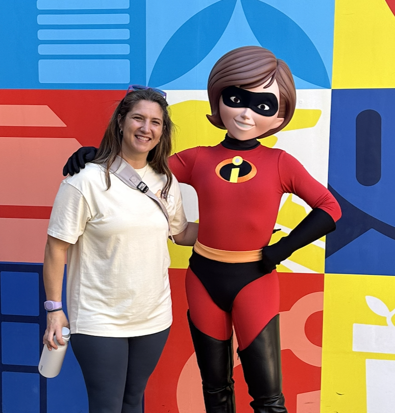 Danielle smiling with Mr. Incredible in front of a colorful mural at Disney's Hollywood Studios.
