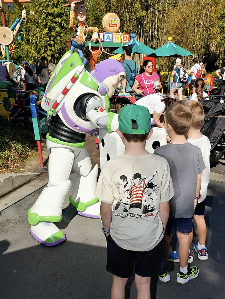 Buzz Lightyear character greeting kids during a parade at a Toy Story-themed area of a Disney park.