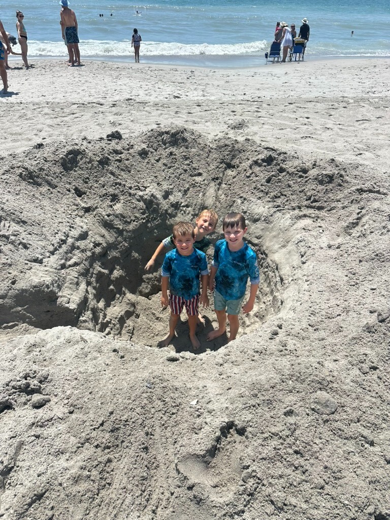 Three boys standing in a large sand hole they dug on the beach in Myrtle Beach