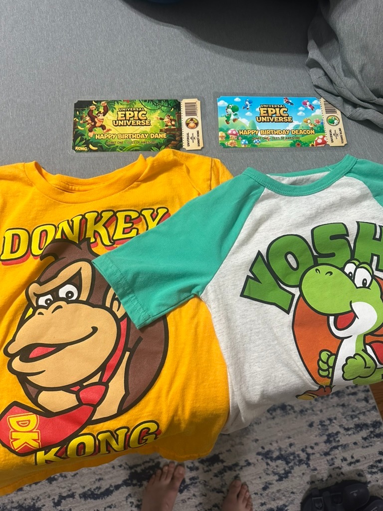 Custom laminated Epic Universe tickets reading "Happy Birthday Dane" and "Happy Birthday Deacon" laid on top of Donkey Kong and Yoshi t-shirts