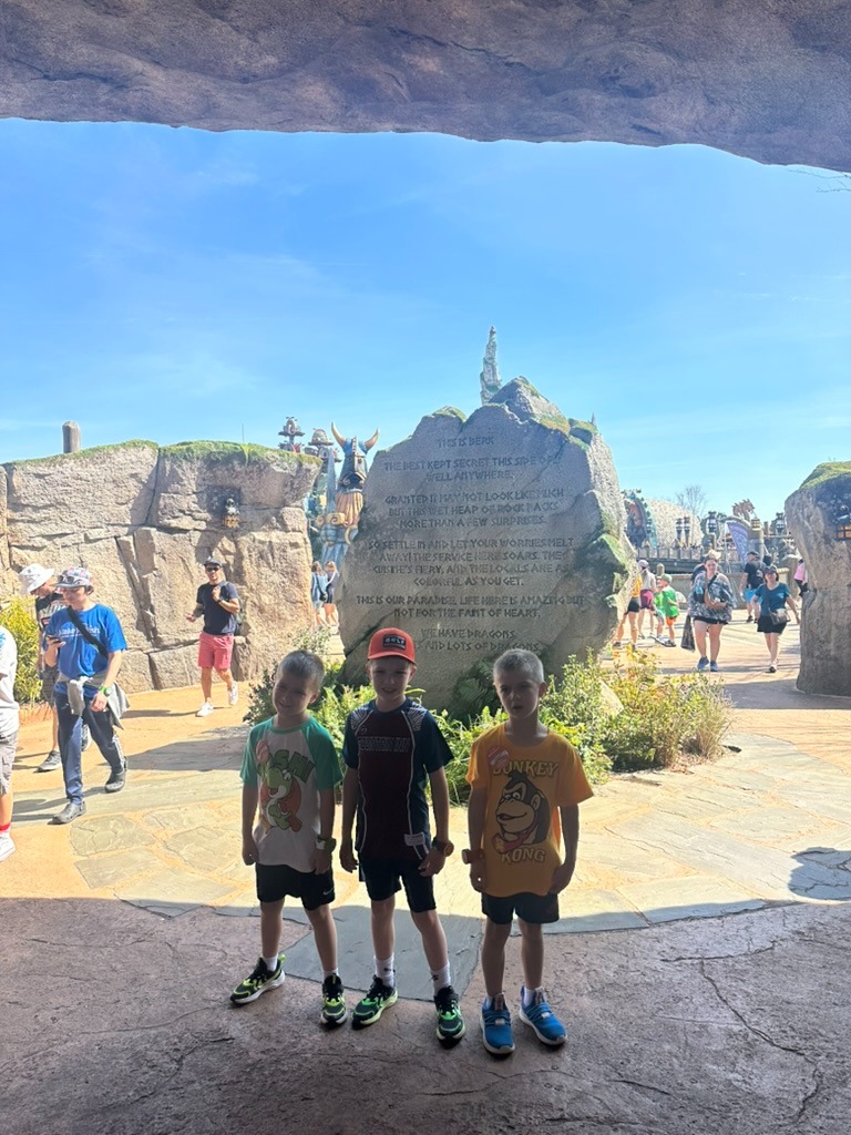 The Isle of Berk entrance at Epic Universe, with towering rock formations and three boys standing near the land's stone entrance plaque