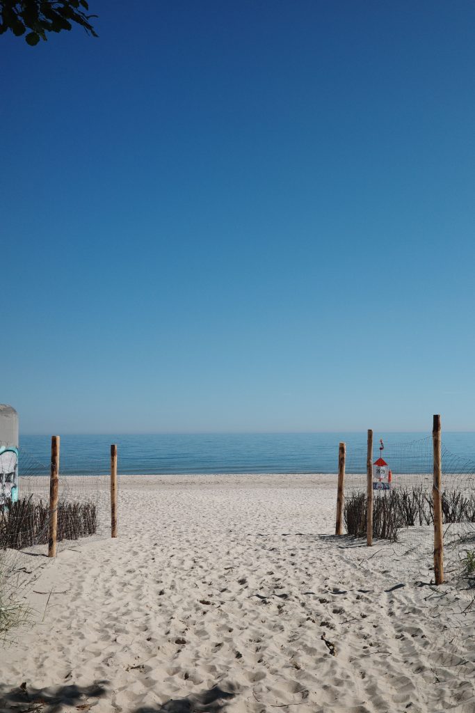 Wooden fence posts leading to a calm ocean beach with soft dune grass, representing a peaceful coastal getaway.